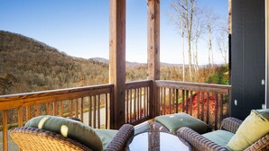 A wooden deck with wicker furniture and cushions, overlooking a hilly landscape. - Wintergreens R611- Mtn Condo/View, Gated Resort, Indoor/Outdoor Pools & Hot Tub (Banner Elk)