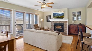 A living room with a fireplace, a ceiling fan, and a TV mounted above it. - Wintergreens R611- Mtn Condo/View, Gated Resort, Indoor/Outdoor Pools & Hot Tub (Banner Elk)