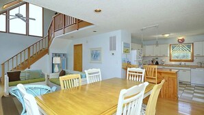 A spacious living area with a wooden dining table, white chairs, a staircase, and a kitchen area. - Fabulous sunsets! (Kitty Hawk)