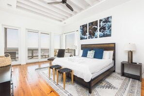 Et rummeligt soveværelse med en stor seng, ventilator i loftet og havudsigt gennem skydedørene.