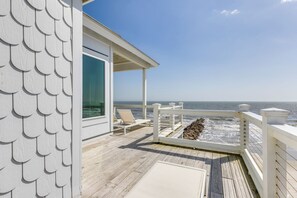 A wooden deck with a railing, a covered seating area, and a view of the ocean.