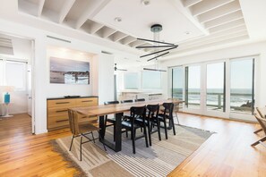 Et moderne interiør med spiseplads, et køkken og en stor skydedør, der fører til en balkon med havudsigt.