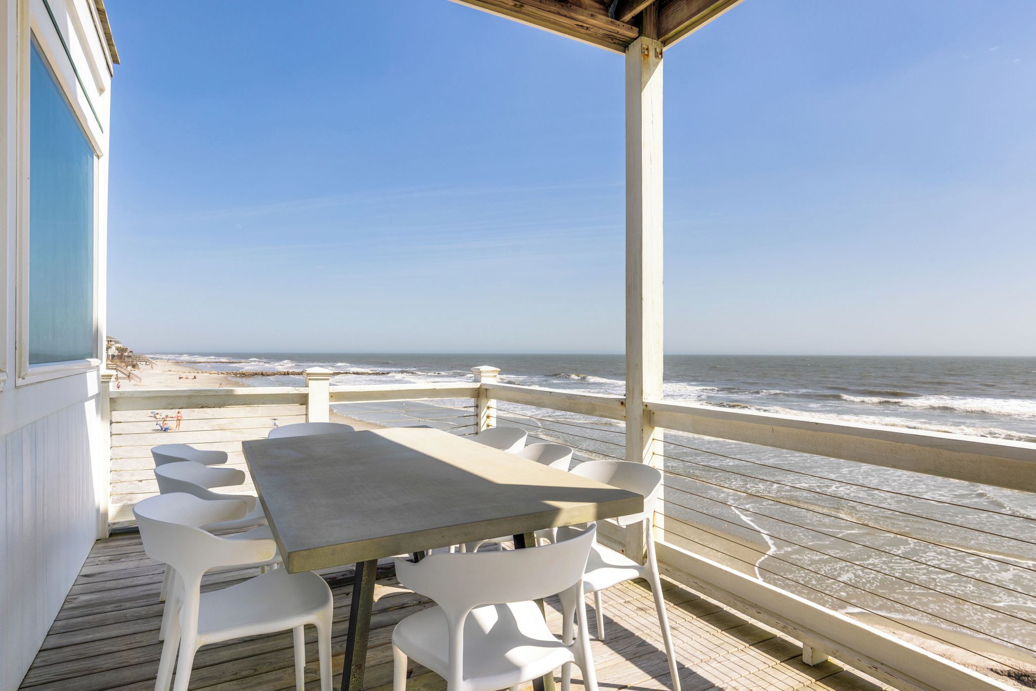 An outdoor patio with a table and chairs, overlooking the beach and ocean.