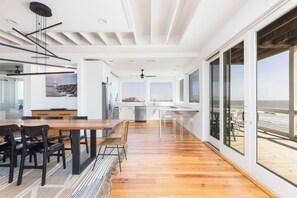 A modern kitchen with a large island, wooden flooring, and a view of the beach.