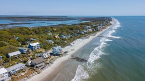 A coastal residential area with houses along the beach, a pier, and a lighthouse in the distance.