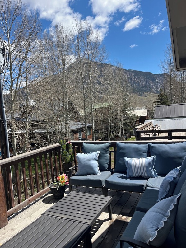 A deck with outdoor furniture, a wooden railing, and a view of mountains.