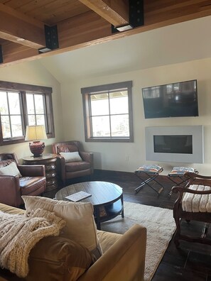 A living room with a fireplace, leather sofas, a coffee table, and a flat-screen TV mounted on the wall. - Elk Cottage In Town! Unique Three Bedroom Townhouse with Mountain Views (Crested Butte)