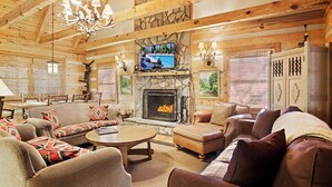 A cozy log cabin interior with a fireplace, comfortable seating, and a television.