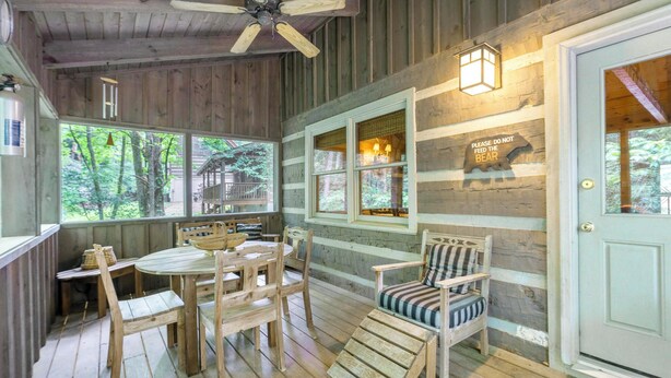 A rustic cabin interior with a wooden dining table, chairs, a bench, and a ceiling fan.