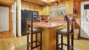 A wooden cabin kitchen with a central island, wooden cabinets, and a refrigerator.