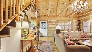 A wooden interior with a staircase, a dining area, and a living room with a sofa and a chandelier.