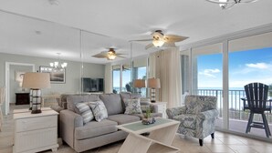Un salon moderne comprenant un canapé, un fauteuil, une table basse et un téléviseur. Il y a un balcon avec vue sur l’océan.