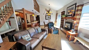 A cozy living room with a leather sofa, wooden coffee table, and a fireplace. A staircase leads to an upper level, and a dining area is visible in the background. - Peak 9 - Walk to Ski Slopes & Main St - Hot Tubs, Pool, Fireplace (Breckenridge)