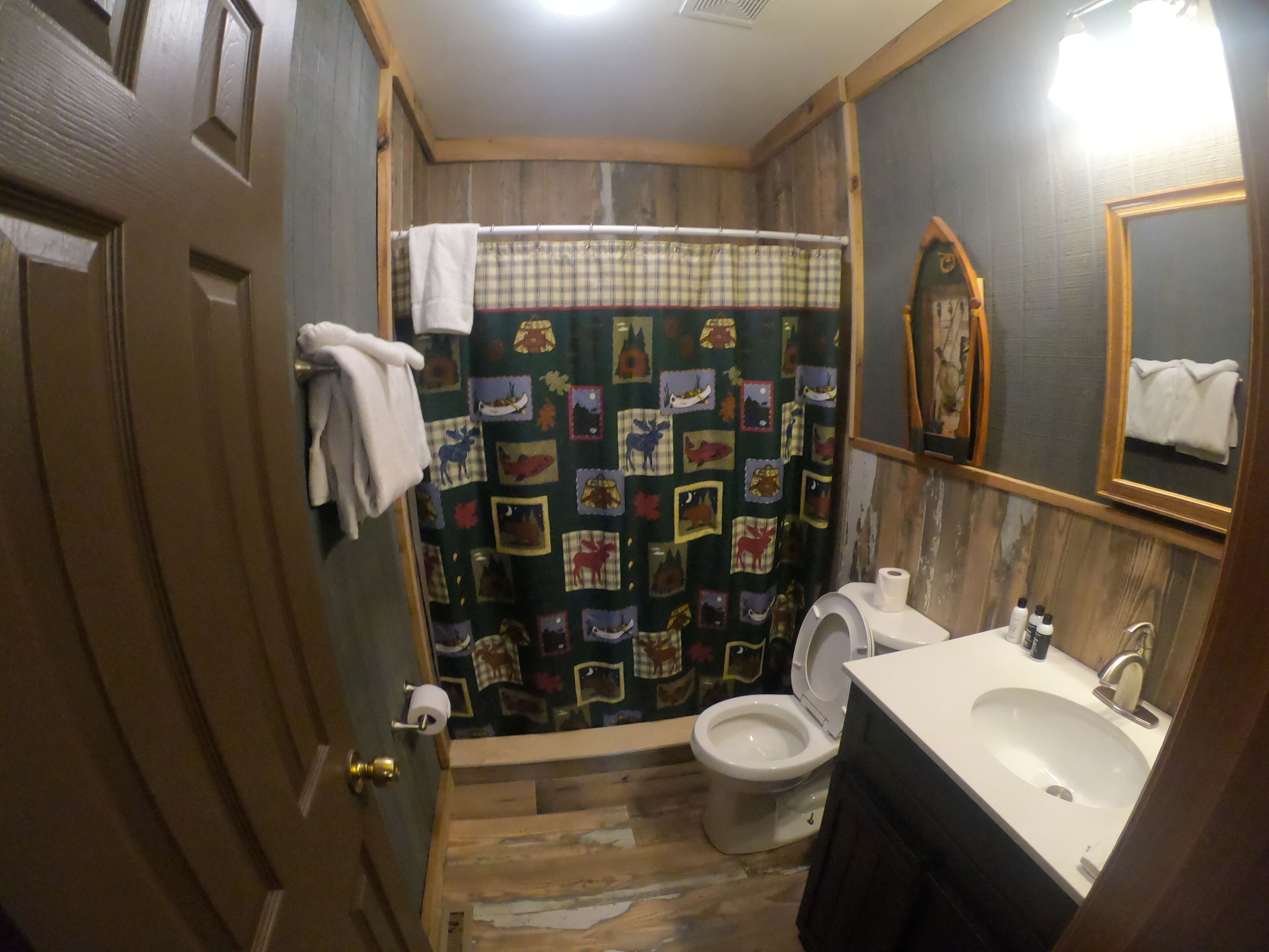 Une salle de bain avec un plancher en bois, des toilettes, un lavabo et un rideau de douche à motifs patchwork.