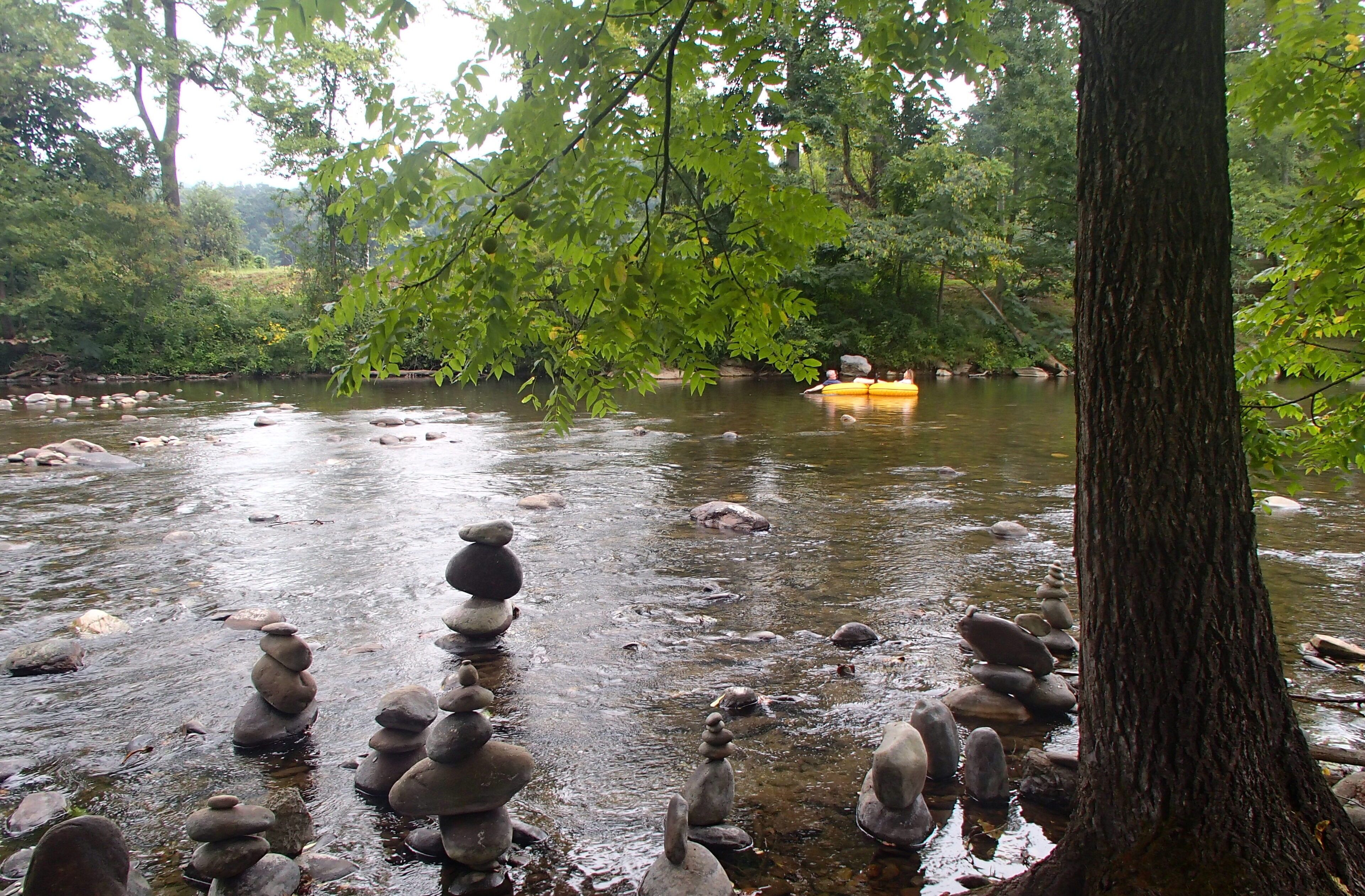 A river with stacked stones and a yellow raft in the background.