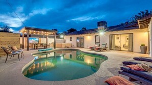 A modern outdoor pool area with lounge chairs and a covered seating area.