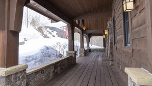 Eine hölzerne Veranda mit Steinwänden und Holzboden, die zu einem Gebäude mit Fenstern und Säulen aus Stein führt.