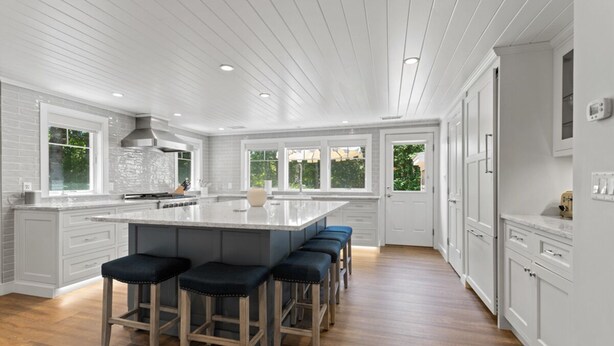 A modern kitchen with a large island, bar stools, and white cabinetry.