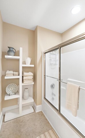 A bathroom with a glass shower enclosure, white shelves with towels and a vase, and a beige wall. - Grand Oaks A1- Mountain Condo, Gated Resort, Indoor/Outdoor Pools & Hot Tub (Boone)