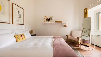 Un dormitorio ordenado con una cama, una silla, una estantería con flores y un espejo.