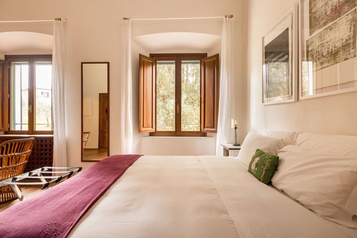 Un dormitorio con una cama grande, una silla de madera, un espejo y una ventana con cortinas.
