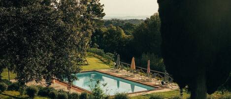 Una piscina rectangular rodeada de césped cuidado y árboles, con una vista despejada del paisaje al fondo.