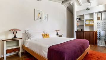 Une chambre à coucher comprenant un lit, des tables de chevet, une commode, une étagère avec des objets décoratifs et un luminaire suspendu.