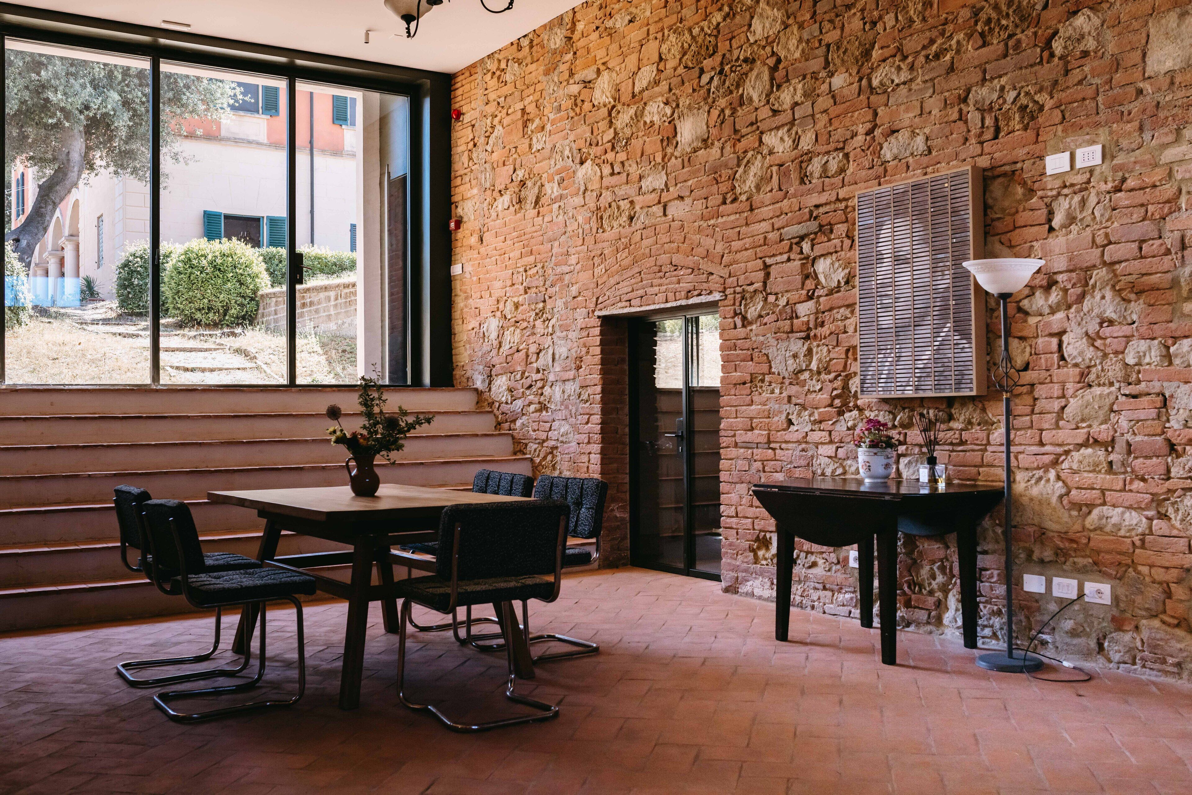 A dining area with a brick wall, a large window, and a table with chairs.