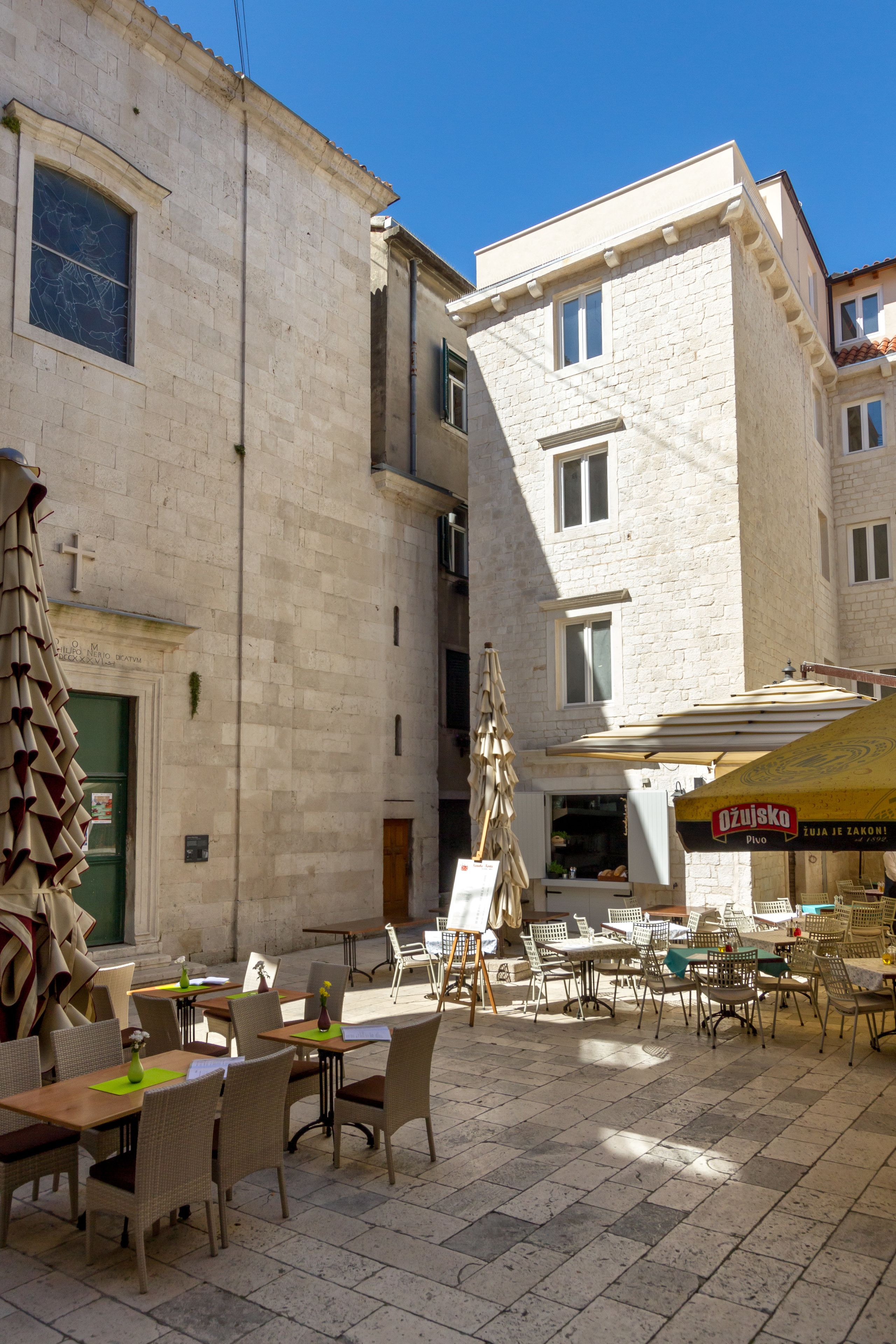 Un caffè all'aperto con tavoli e sedie, un edificio con facciata in pietra e un cartello per un ristorante.