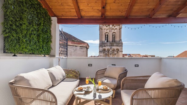 A rooftop terrace with wicker furniture, a table with breakfast items, and a view of a historic tower. - Luxury Apartment Matkovic (Split)