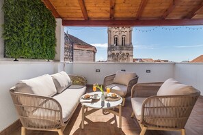 Een terras op het dak met rieten meubilair, een tafel met ontbijtartikelen en uitzicht op een historische toren.