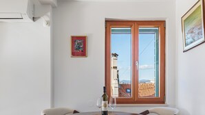 A dining area with a round table, six chairs, a wine bottle, and a glass. There is a window with a view of buildings and a door with a wooden frame. - Luxury Apartment Matkovic (Split)