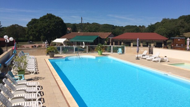 A swimming pool with lounge chairs and umbrellas, surrounded by buildings and trees. - Les Sentiers du Causse  (Lentillac-du-Causse)