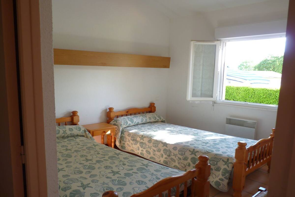Ein Schlafzimmer mit zwei Einzelbetten, einem Holz-Kopfteil, einem kleinen Nachttisch und einem Fenster mit Blick ins Grüne.