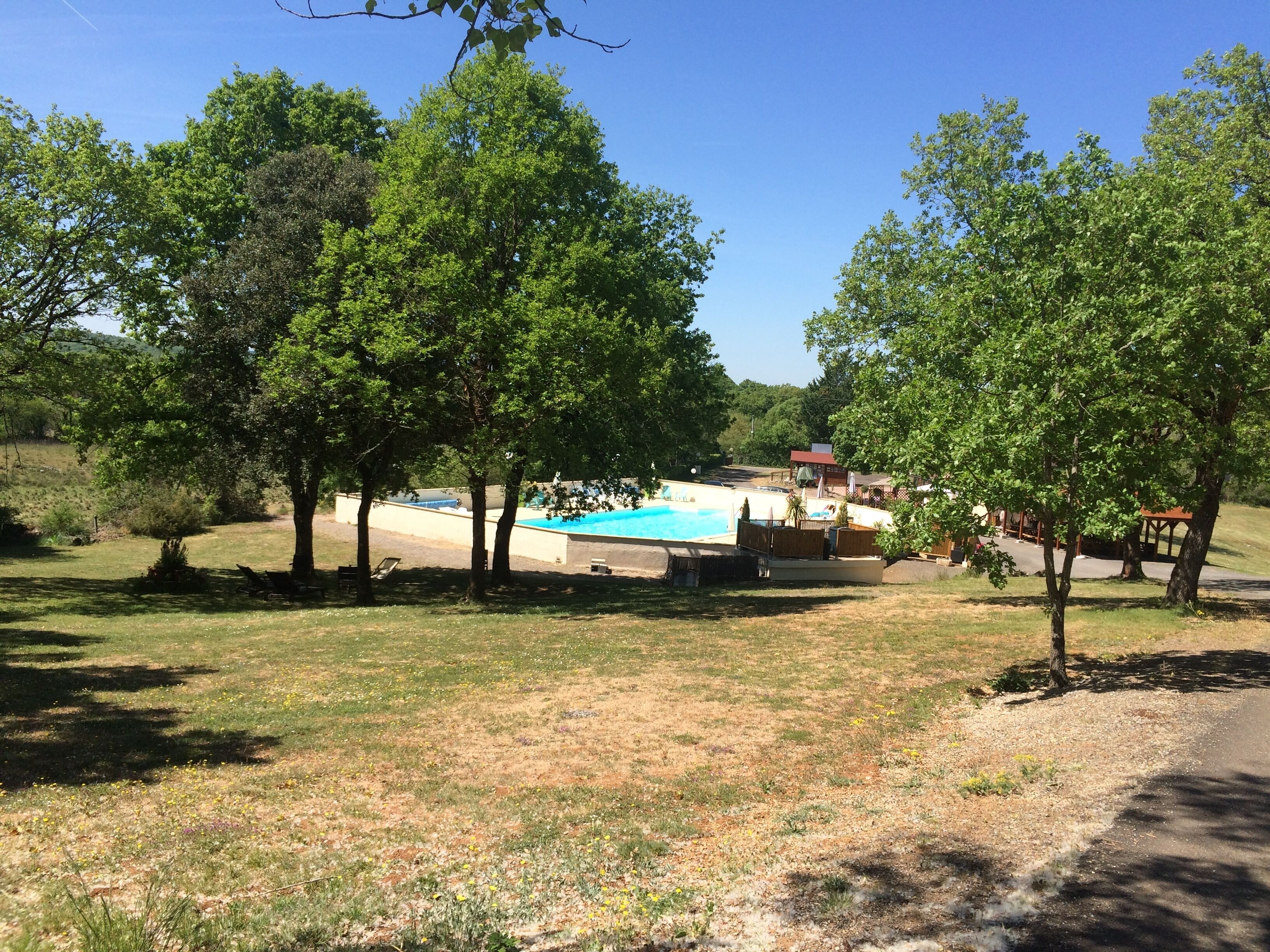 A pool area surrounded by trees, with a building in the background.