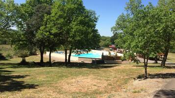 A pool area surrounded by trees, with a building in the background.