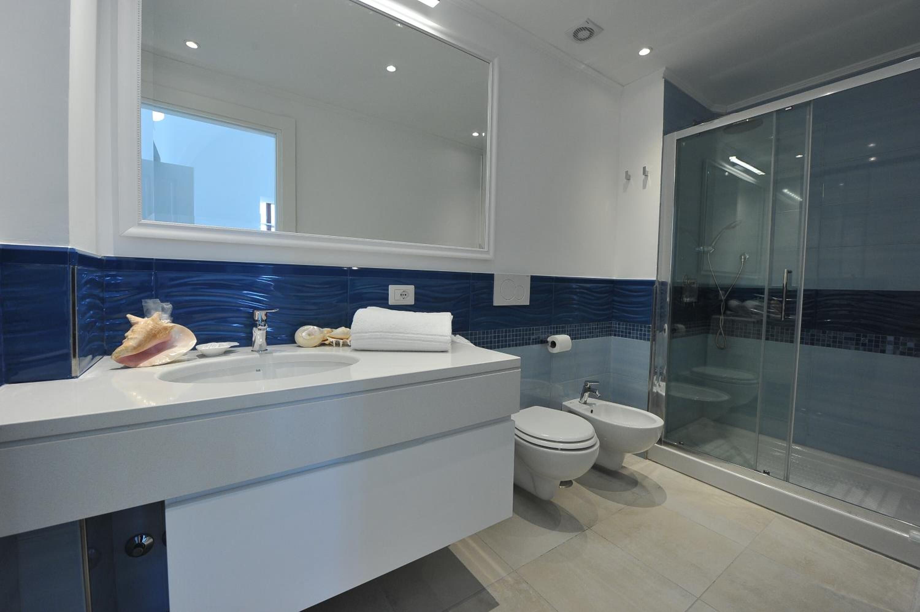 Een moderne badkamer met een grote spiegel, een witte wastafel en een douche met glazen wanden.