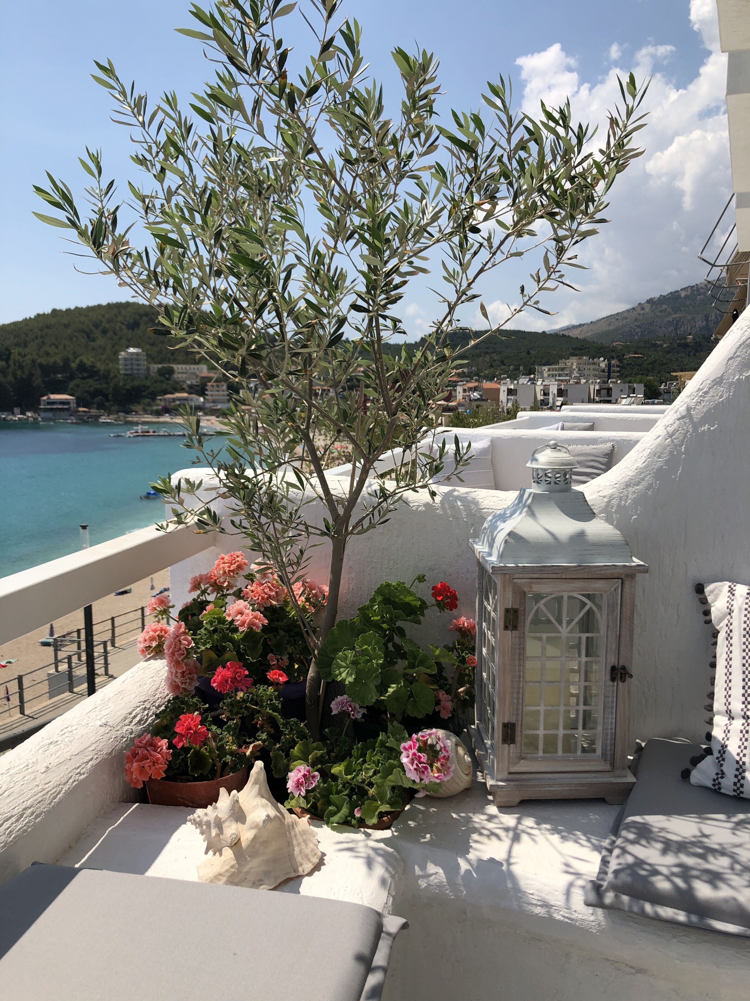 Un balcon avec une balustrade blanche, une petite lanterne blanche et un pot de fleurs orné de fleurs roses.