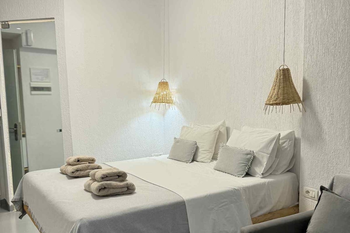 Ein modernes Schlafzimmer mit einem großen Bett, zwei Nachttischlampen, einem Sessel und einer sichtbaren Tür.