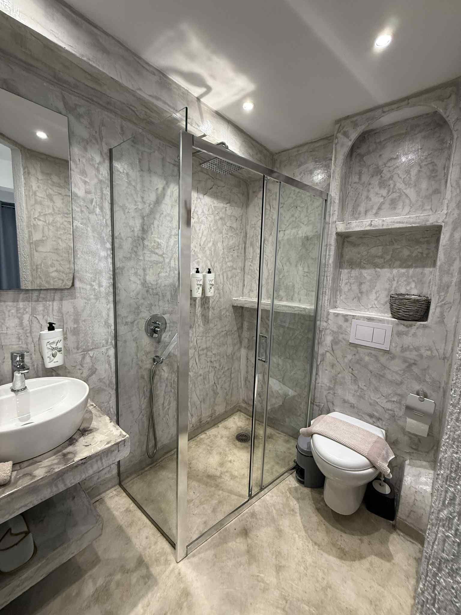 A bathroom with a marble sink, a glass-enclosed shower, and a toilet.