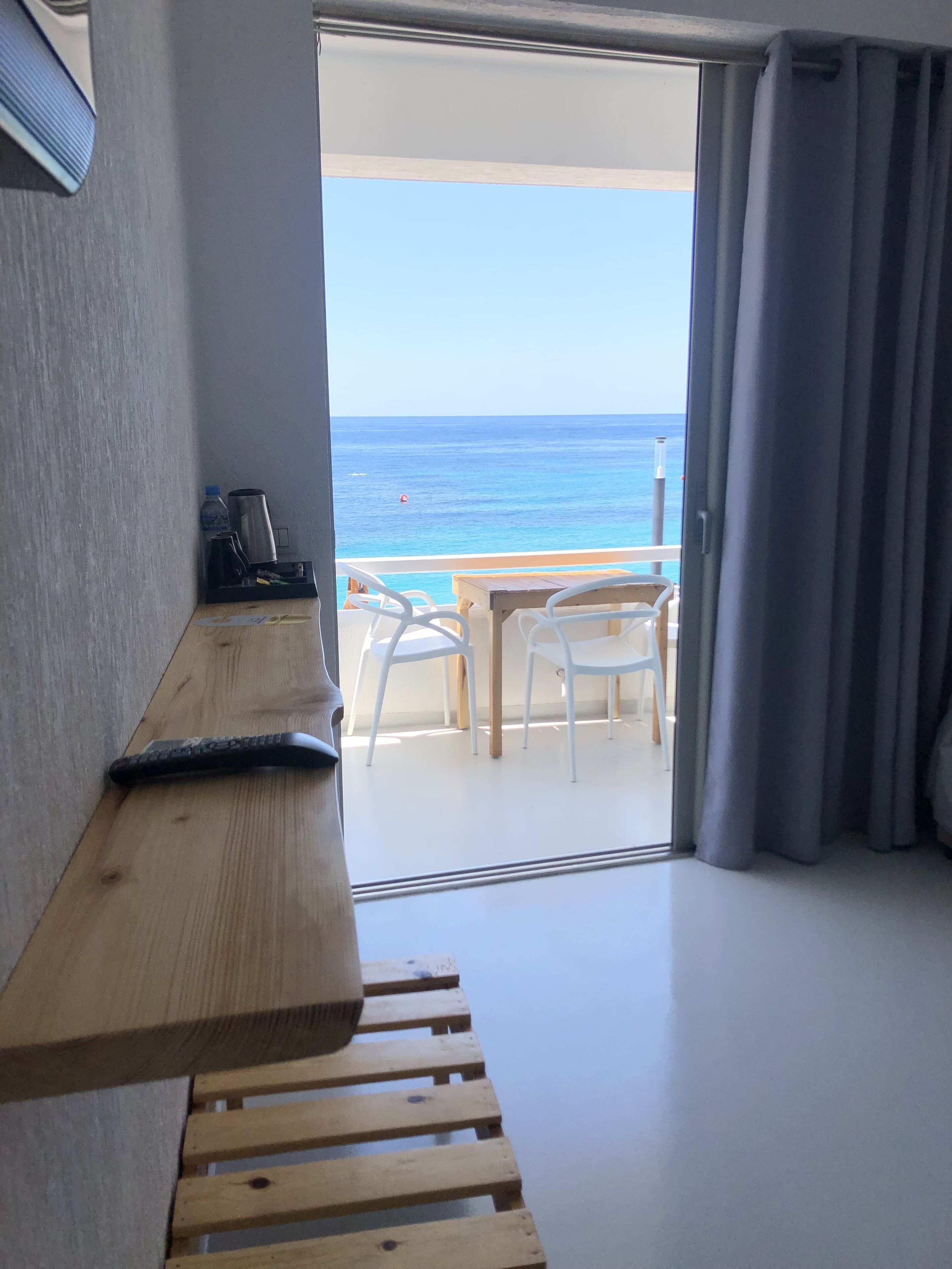 Ein Zimmer mit einer hölzernen Bank, einem Tisch und Blick auf das Meer durch eine Glastür.