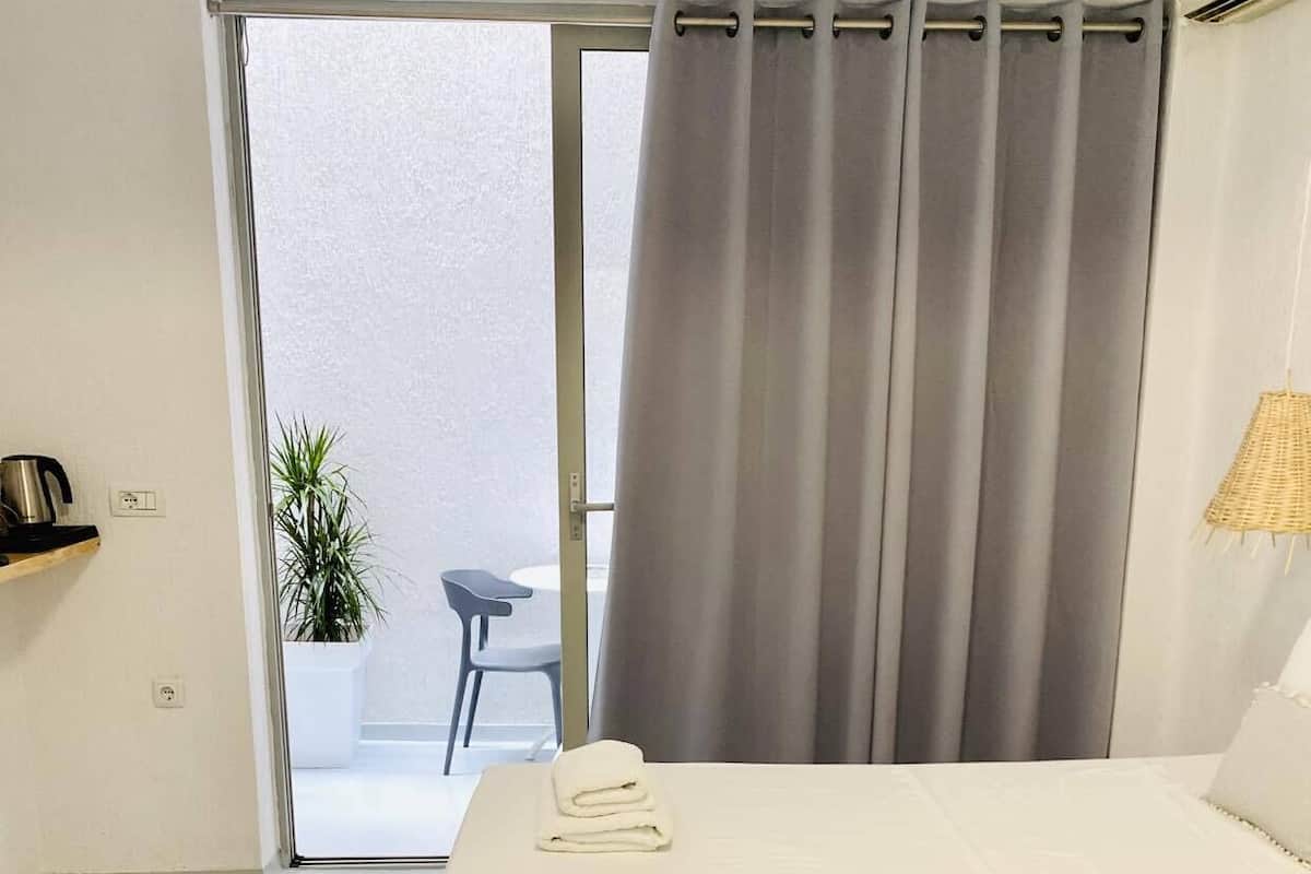 Ein Schlafzimmer mit Bett, Holz-Kopfteil, kleinem Tisch mit Wasserkocher, Stuhl und Topfpflanze.