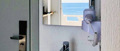 Un baño con lavamanos, espejo y vista al océano a través de una puerta abierta.