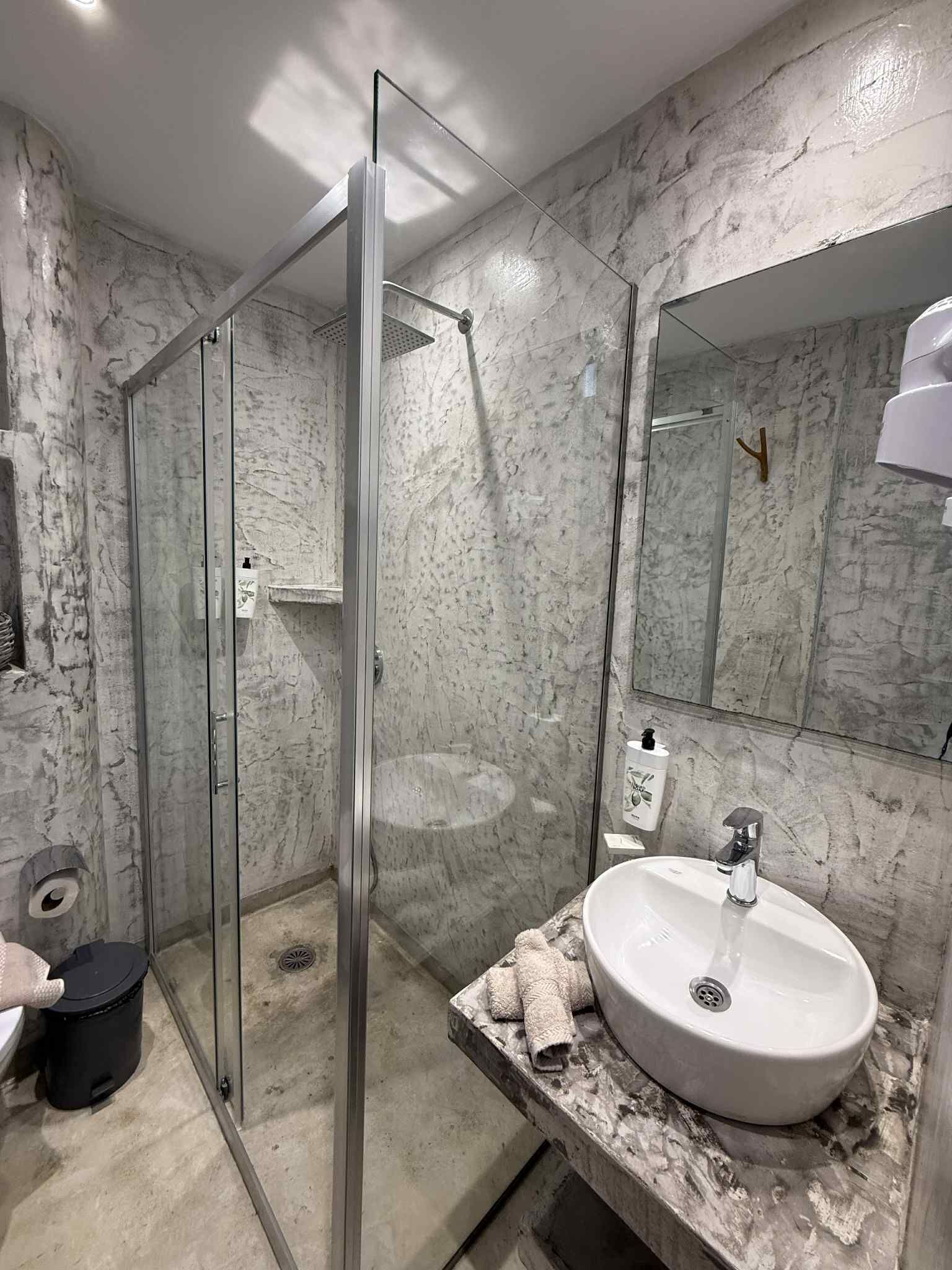 A bathroom with a glass-enclosed shower, a marble sink, and a large mirror.