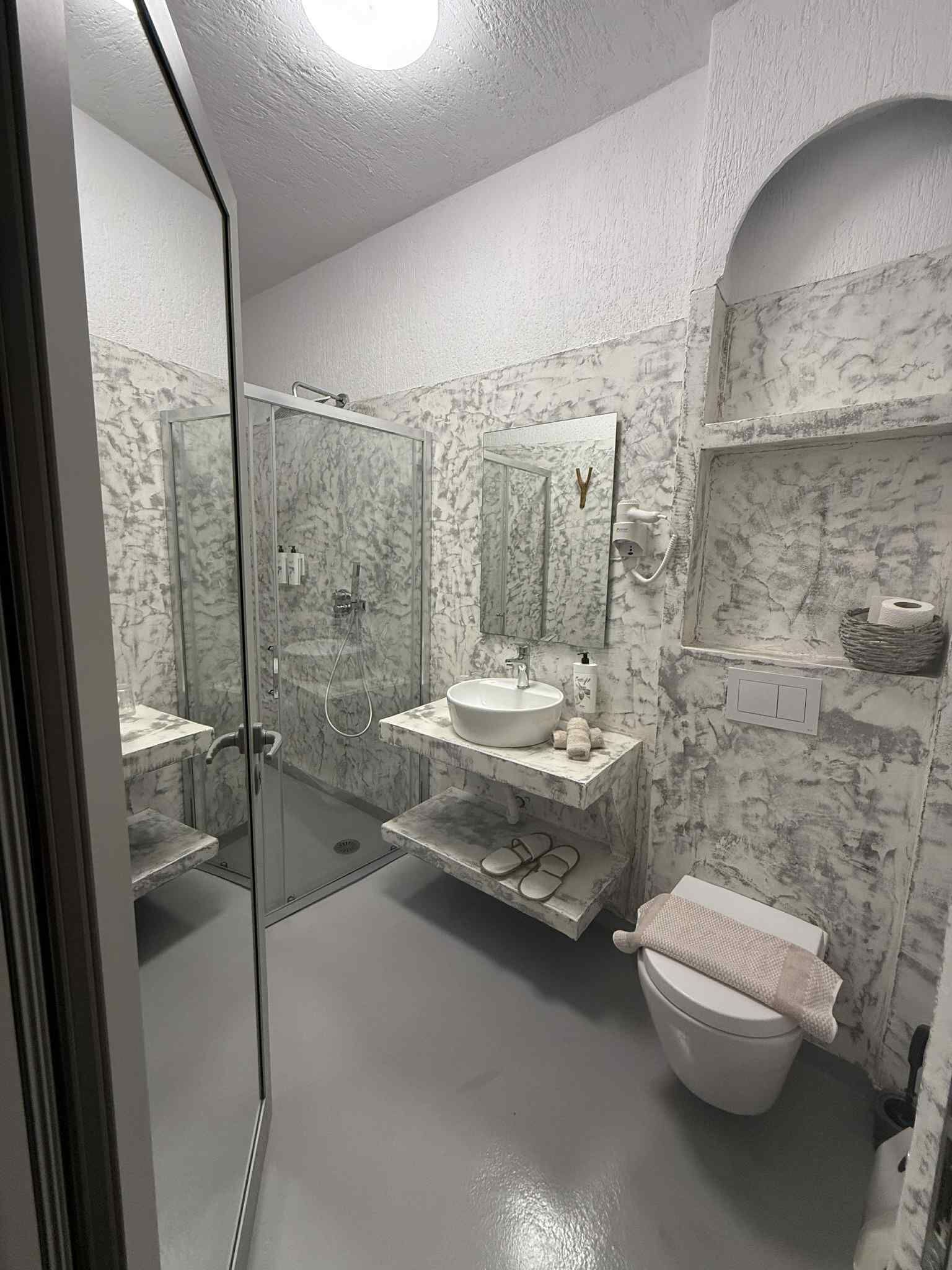 A bathroom with a glass-enclosed shower, a sink with a marble countertop, a toilet, and a mirror above the sink.