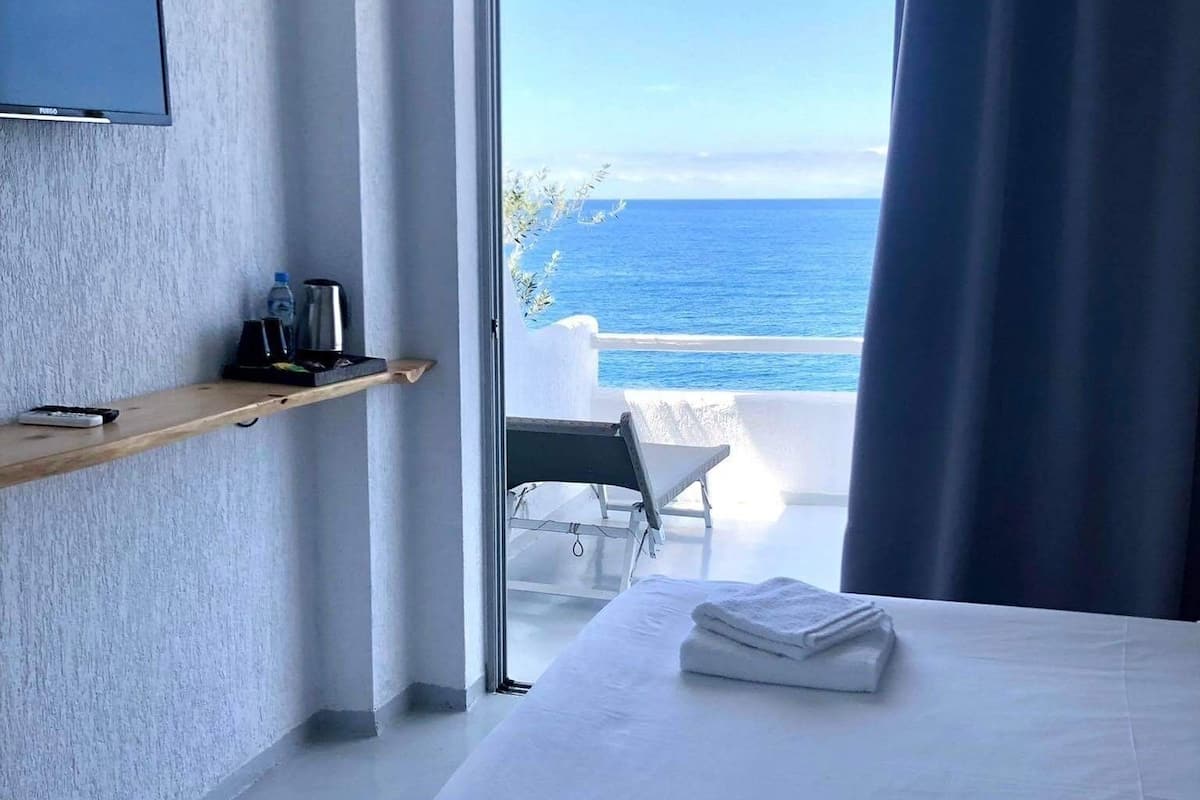 Ein Hotelzimmer mit Bett, Fernseher, Ablagefläche mit Gegenständen und Blick aufs Meer.