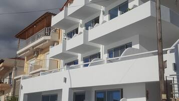 Un edificio de varios pisos con balcones, fachada blanca y una pared de piedra en un lateral.