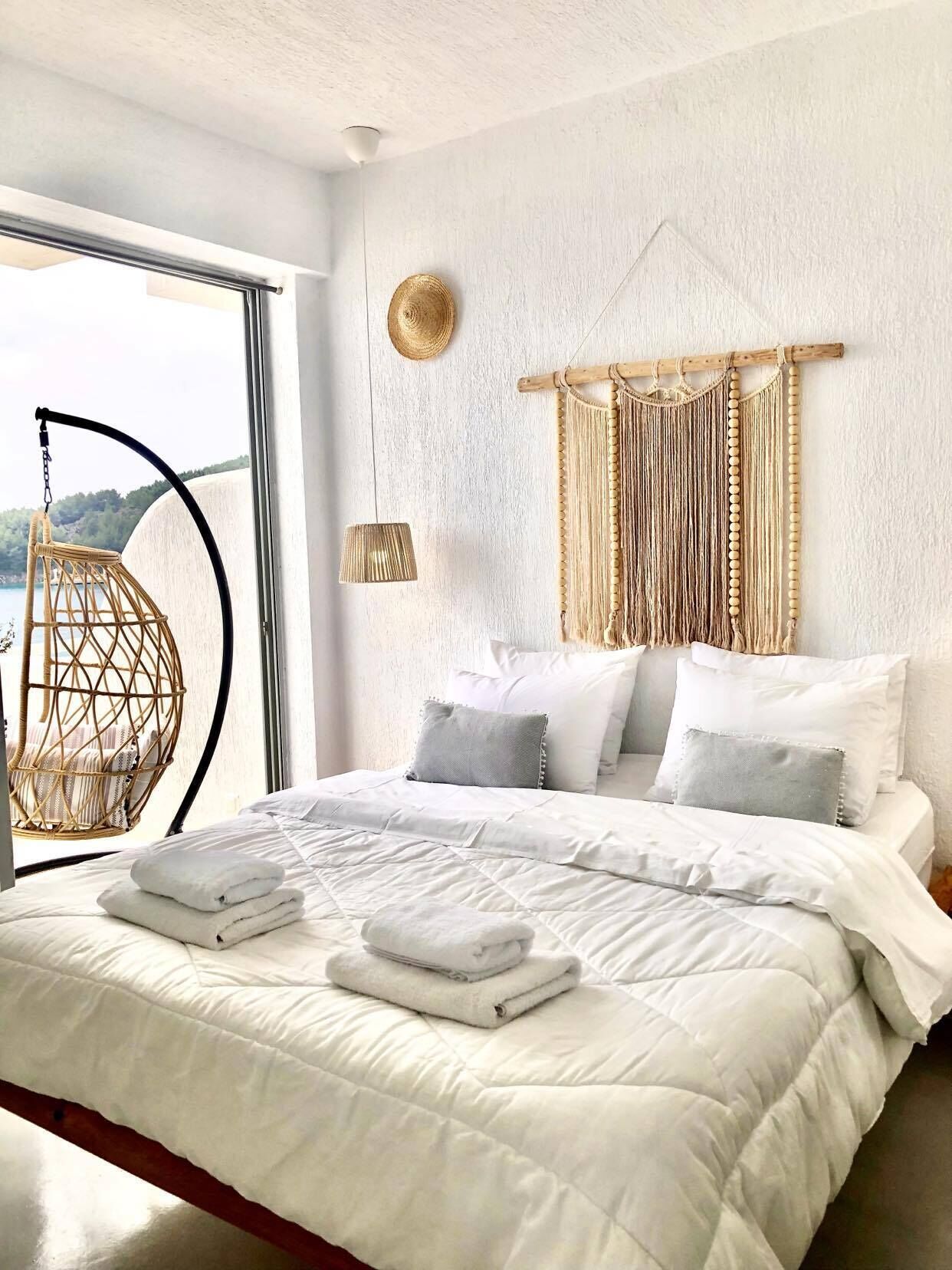 Een slaapkamer met een groot bed, een hangstoel, een macramé wanddecoratie en uitzicht op de omgeving.