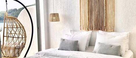 Een slaapkamer met een groot bed, een hangstoel, een macramé wanddecoratie en uitzicht op de omgeving.