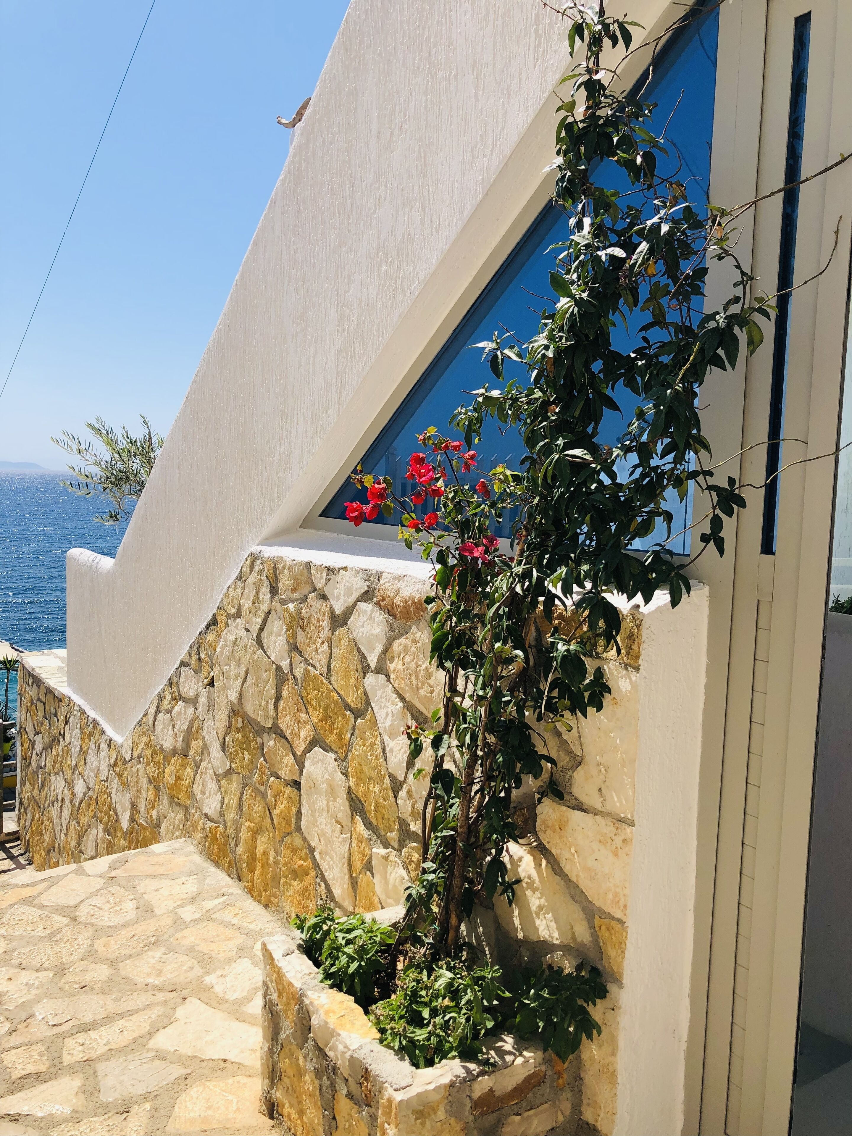 Un bâtiment moderne à la façade en pierre et blanche, avec une fenêtre bleue et une vue sur la mer.